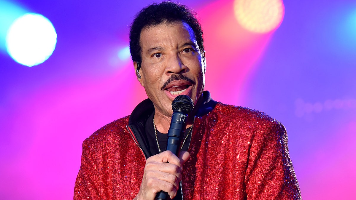 Lionel Richie parle dans le microphone sur scène avec une veste rouge scintillée