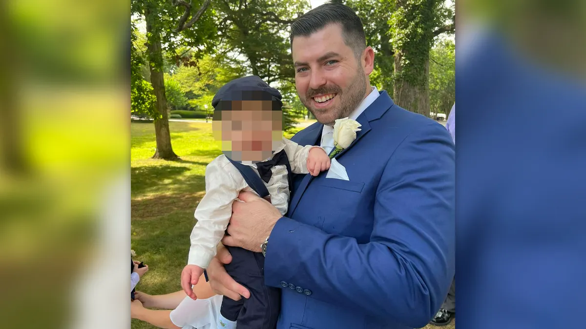 L'agent Jonathan Diller tient un enfant dans ses bras et porte un costume bleu.